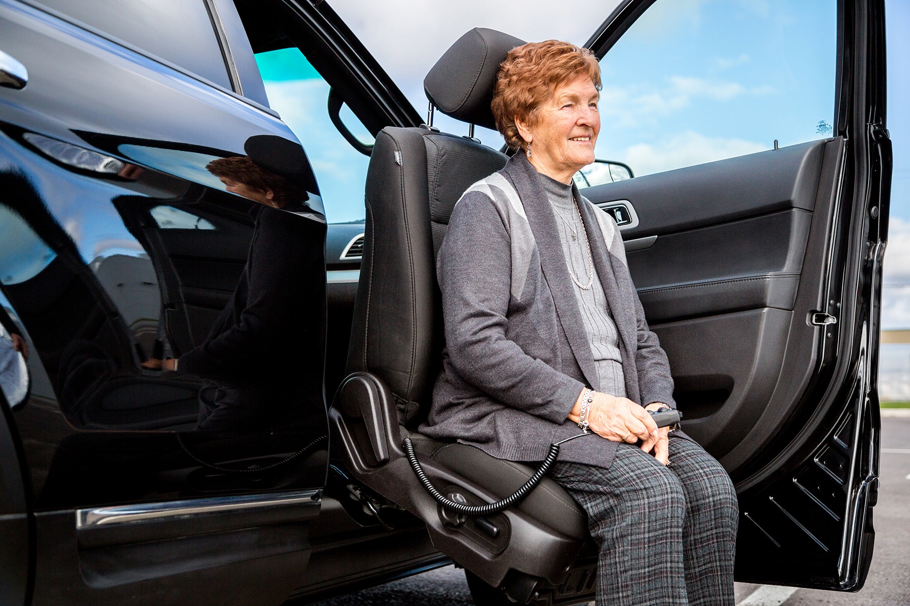 A LINK using the lift-up feature to help an eldery woman stand on the passenger's side of an SUV.