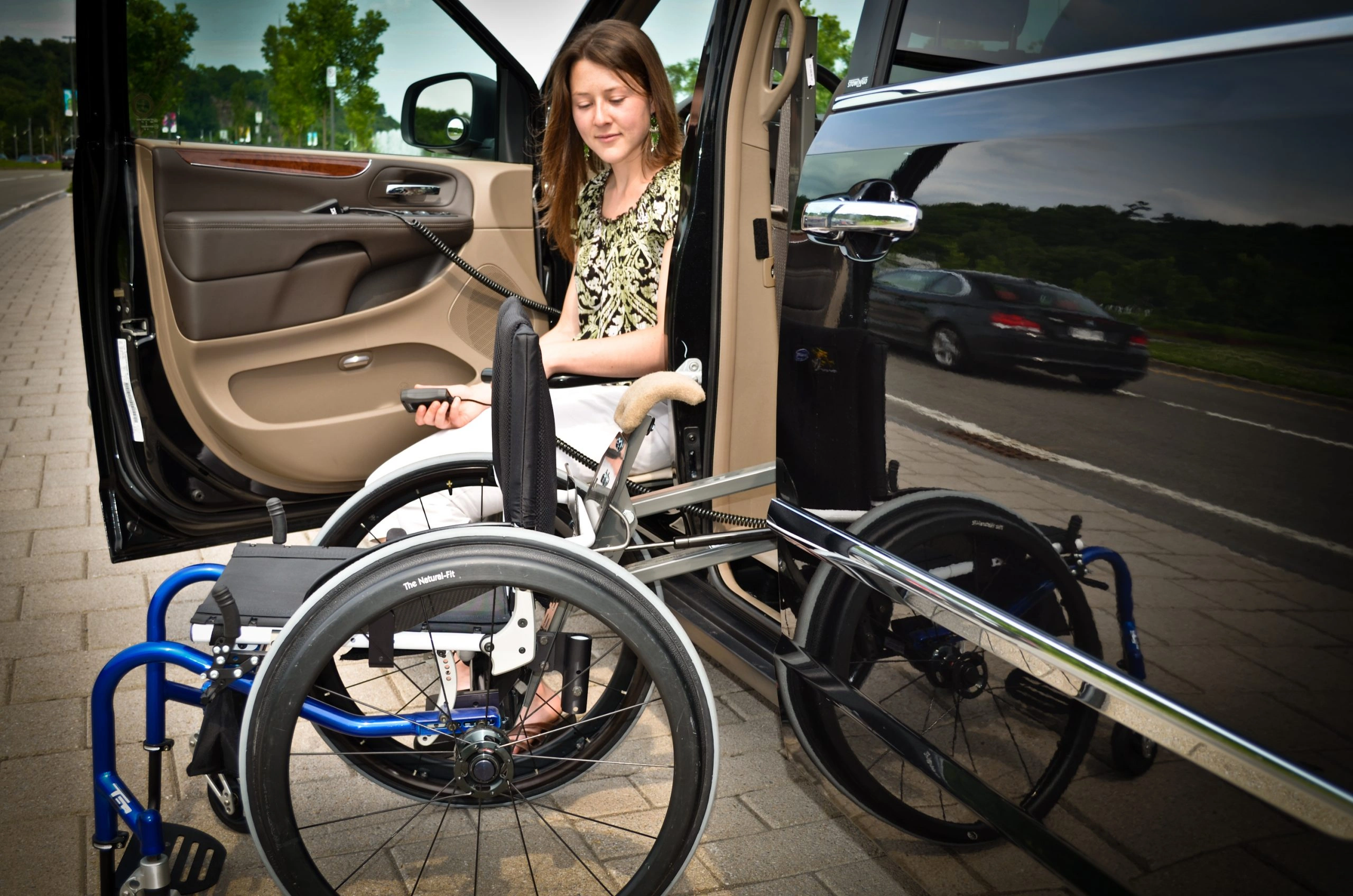 A woman is looking at the SPEEDY-LIFT while seated on an XL-SEAT as it starts to lift her rigid-framed manual wheelchair.